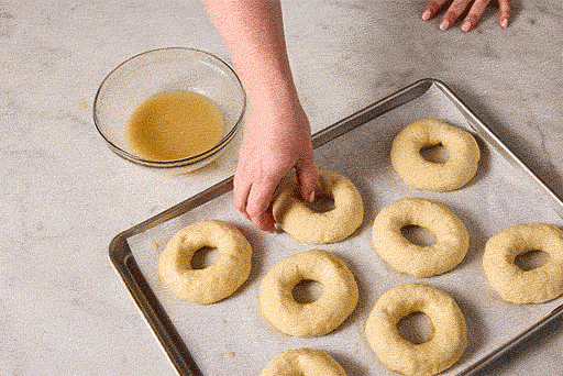 Animated gif of a person dipping formed bagel dough into a bowl of glaze.
