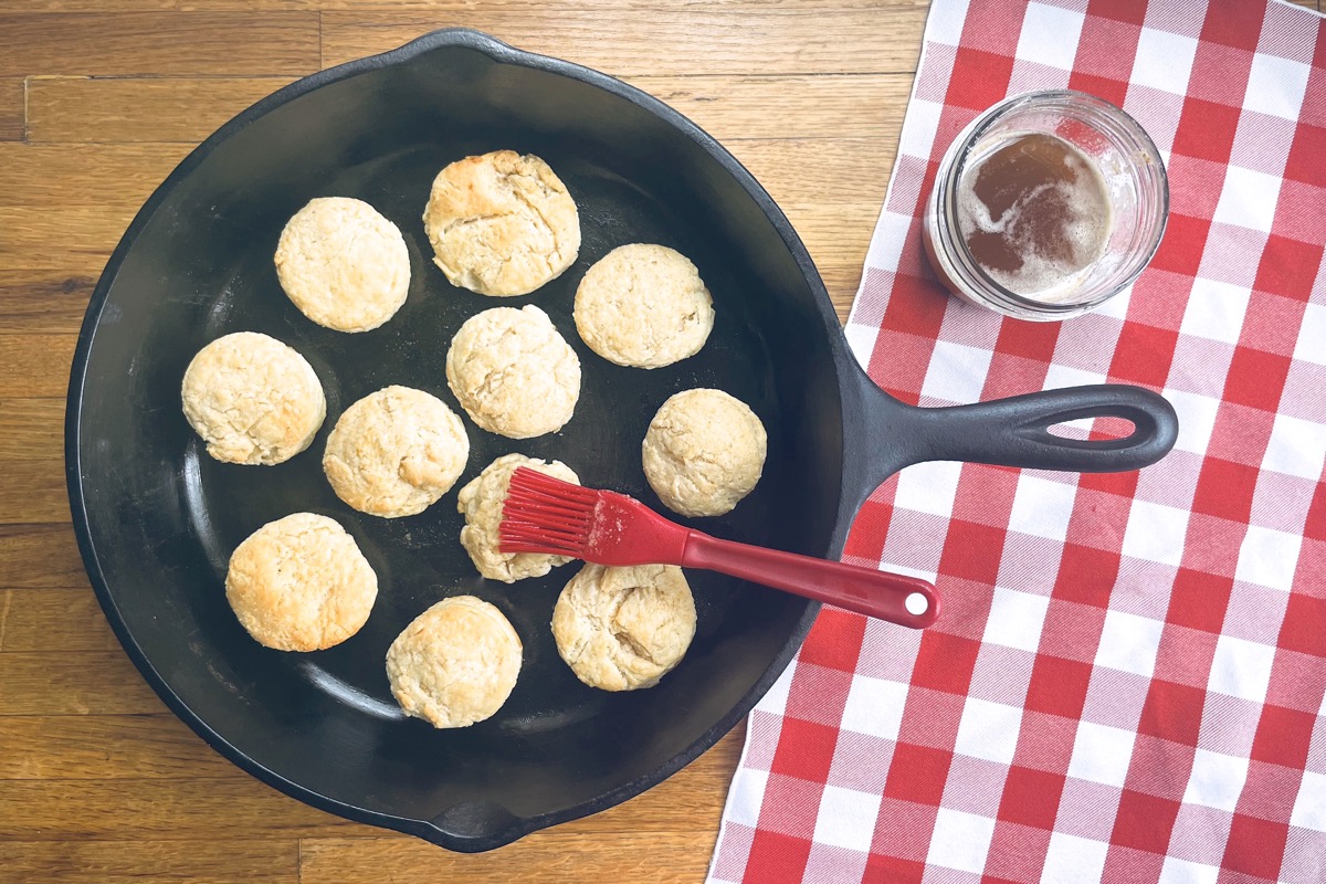 Sourdough biscuits in a cast iron frying pan being brushed with brown butter.