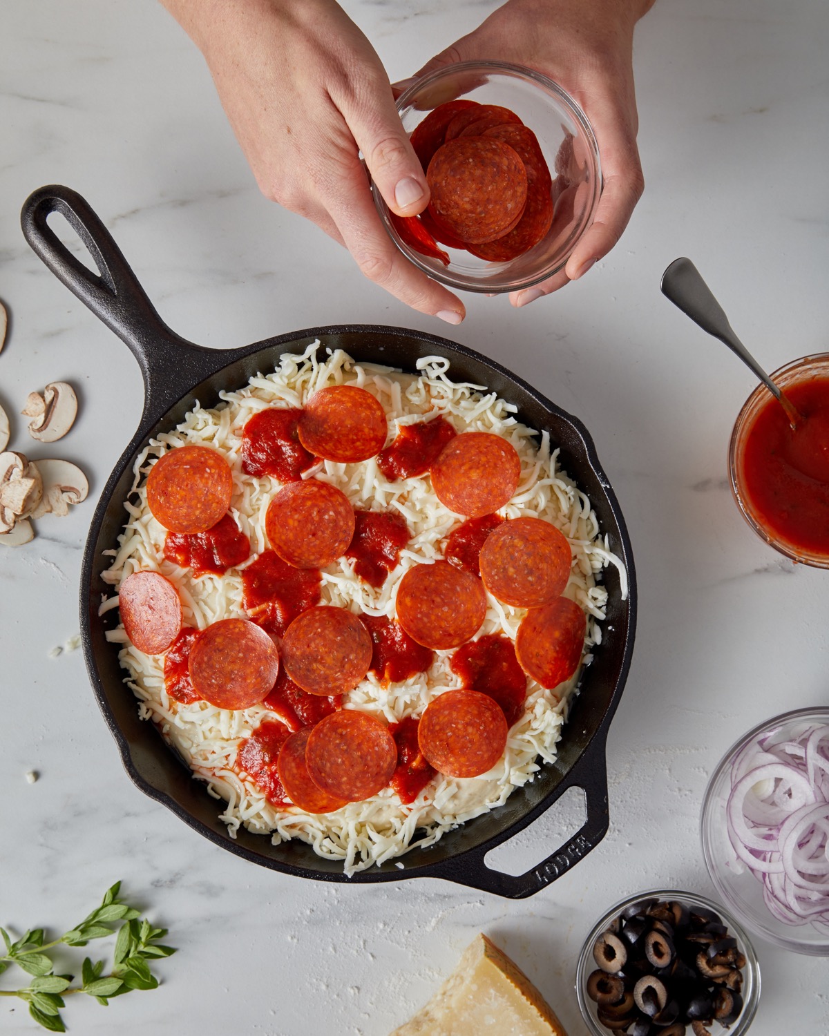 Pepperoni slices being arranged atop a cheese-topped pizza, ready for the oven.
