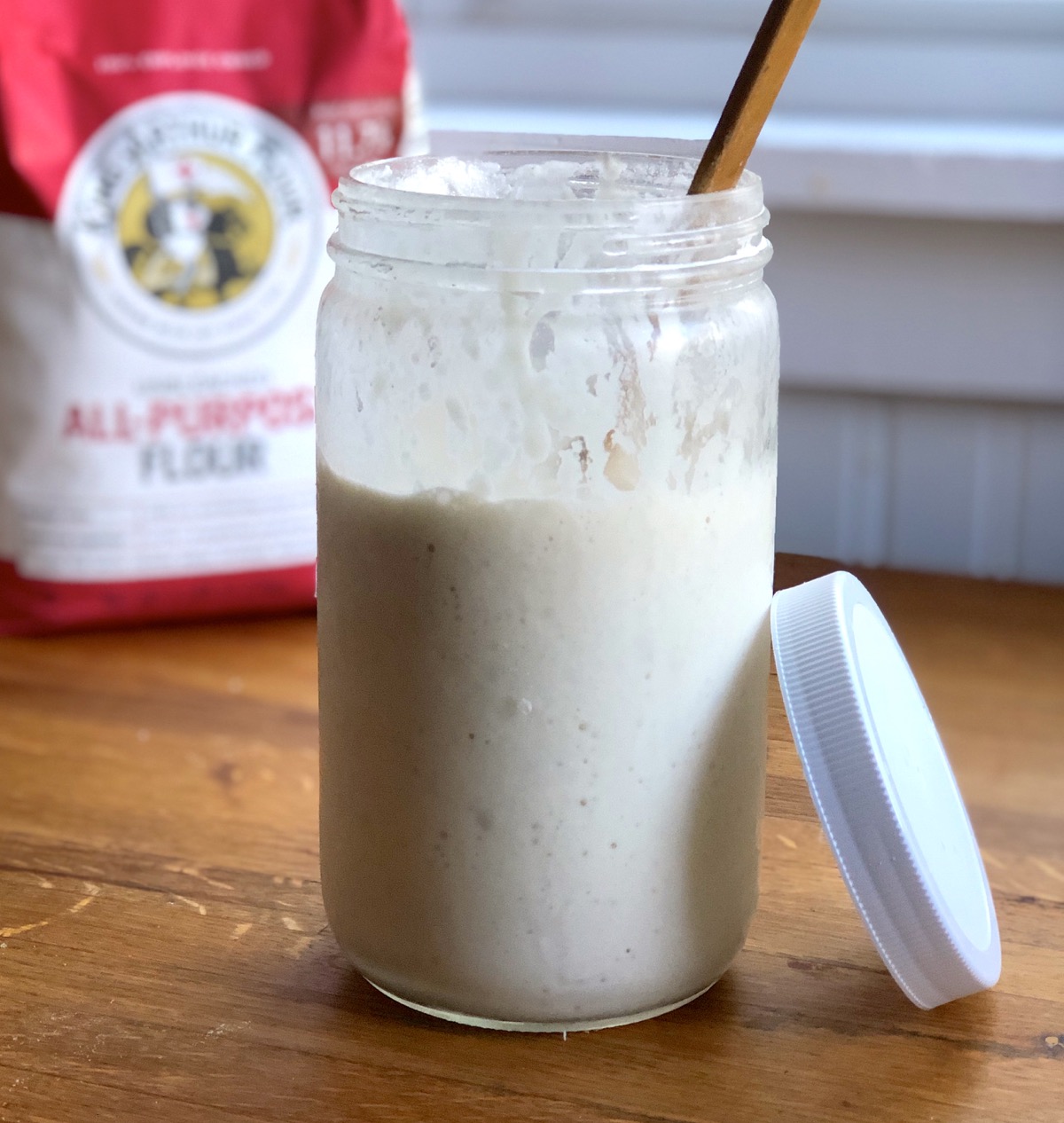Discard sourdough starter in a jar, bag of King Arthur Flour in the back.