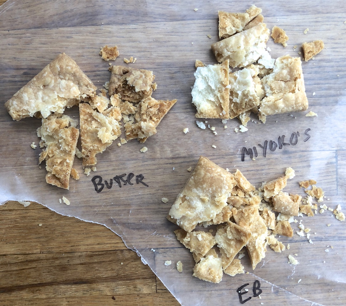 Three small squares of pie pastry made with three types of butter, crushed slightly to show their flaky texture