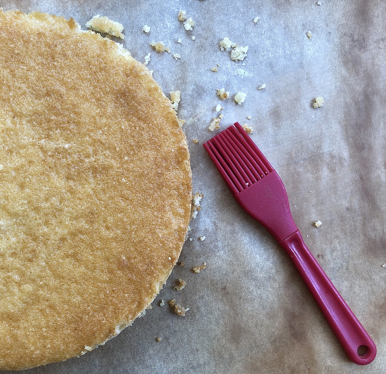 single round layer of yellow cake on a piece of parchment, with pastry brush to brush off crumbs.