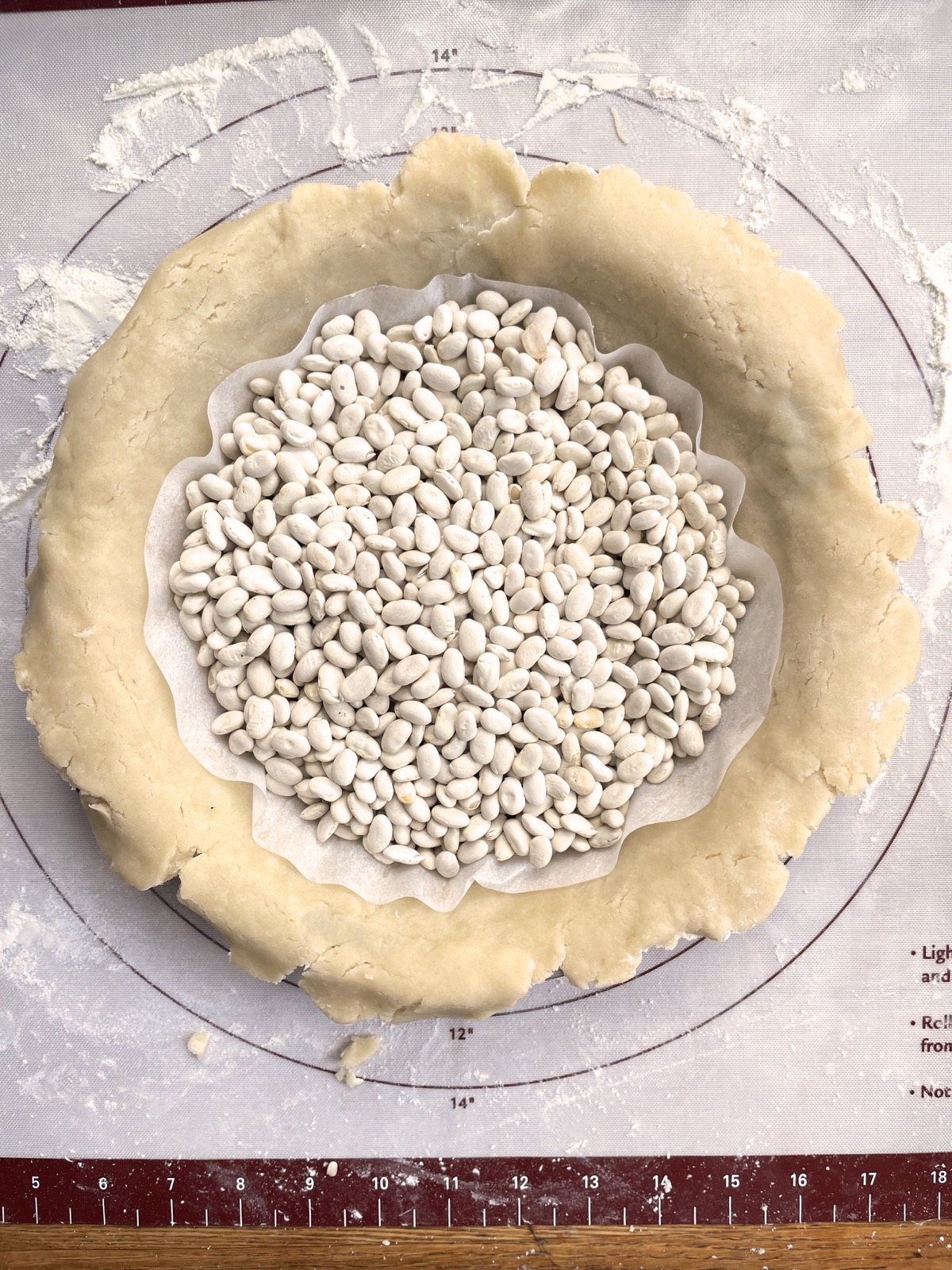 Pie crust in a pan layered with a parchment circle and dried beans, ready to prebake.