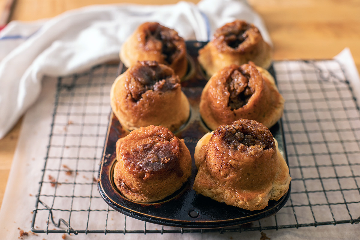 Freshly baked gluten-free cinnamon rolls cooling upside down on a cooling rack, showing off the sticky bottom