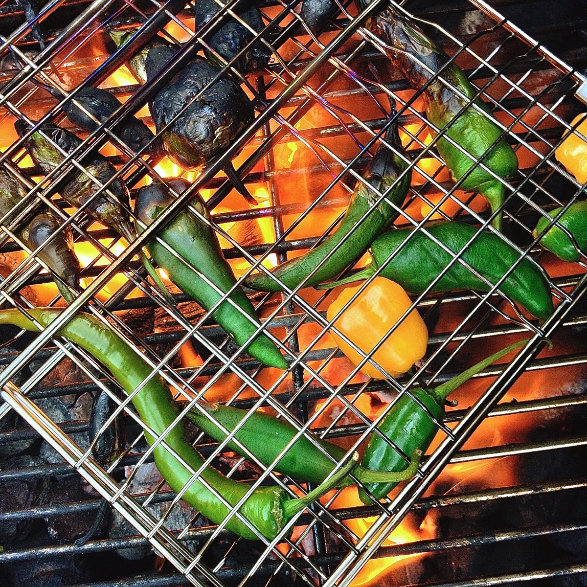 Serrano peppers and small yellow bell peppers charring on an open-flame grill.