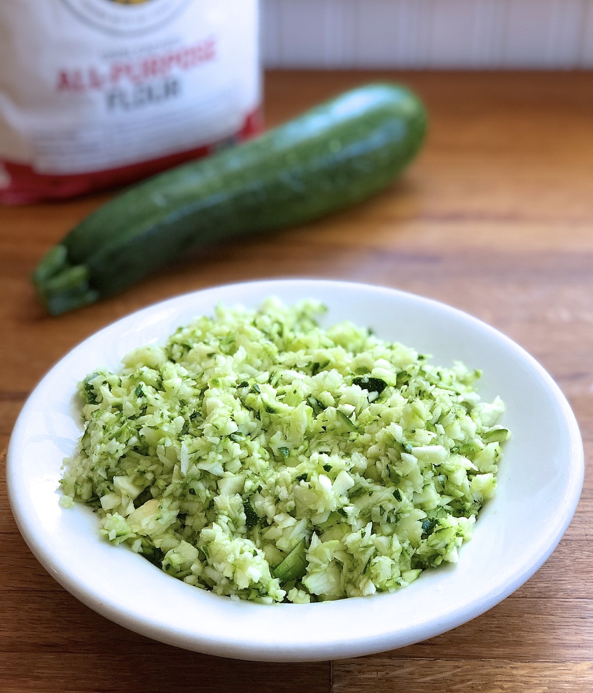 Whole zucchini with a bowl of chopped aucchini.