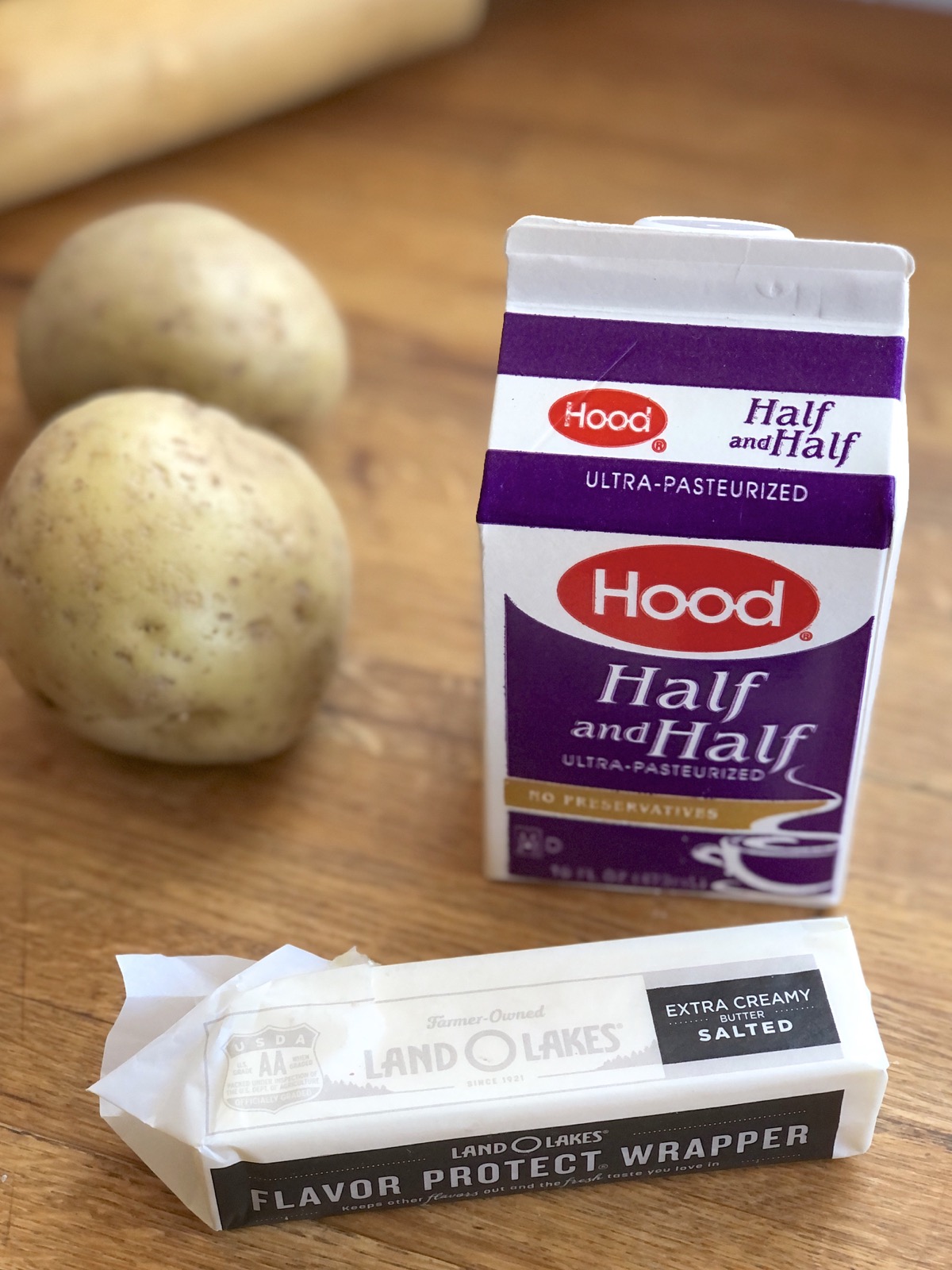 Stick of butter and carton of half and half on a wooden tabletop.