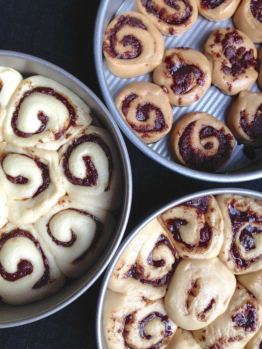 Three batches of cinnamon rolls rising in pans, made with all white flour, 50% white flour, or all whole wheat flour. 