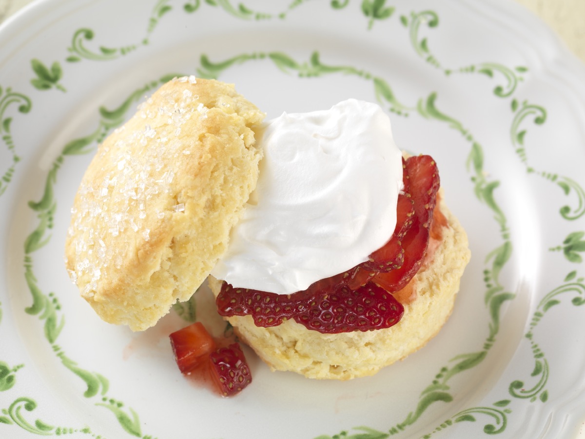 Strawberry shortcake: a biscuit topped with cut berries and whipped cream, all on a saucer.