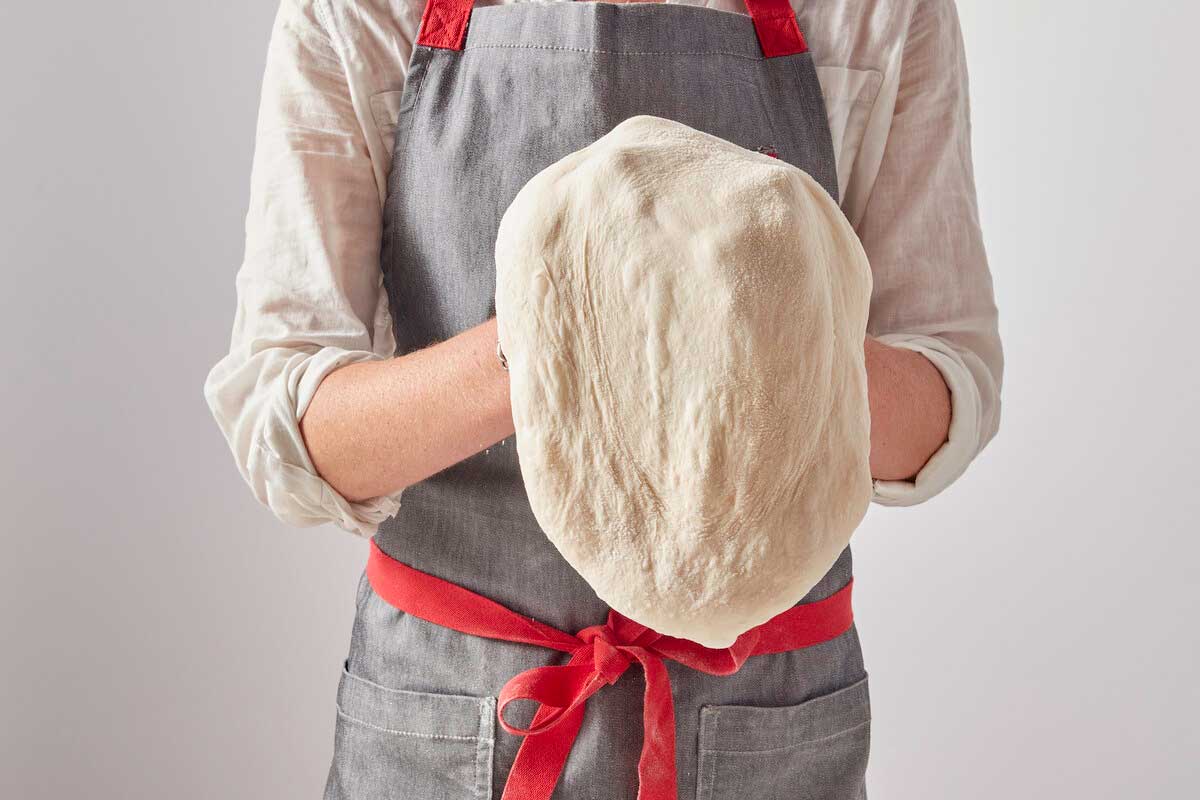 Standing baker shaping dough into a pizza shape