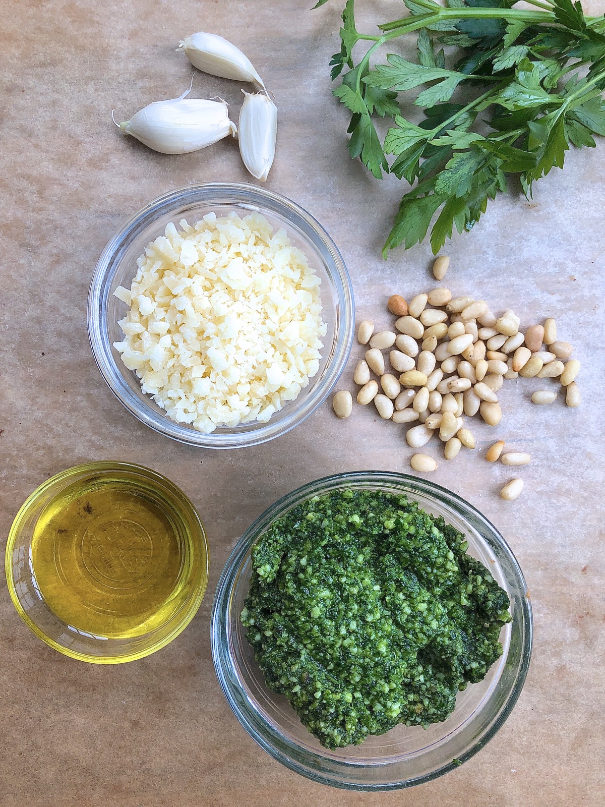 Ingredients for pesto sauce, incouding parsley, grated Parmesan, olive oil, pine nuts, and garlic cloves