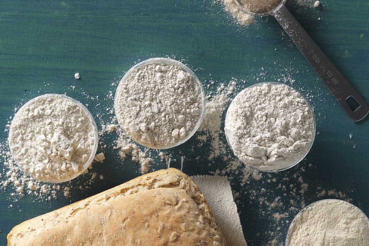 Several small bowls of various rye flours, next to a loaf of rye bread