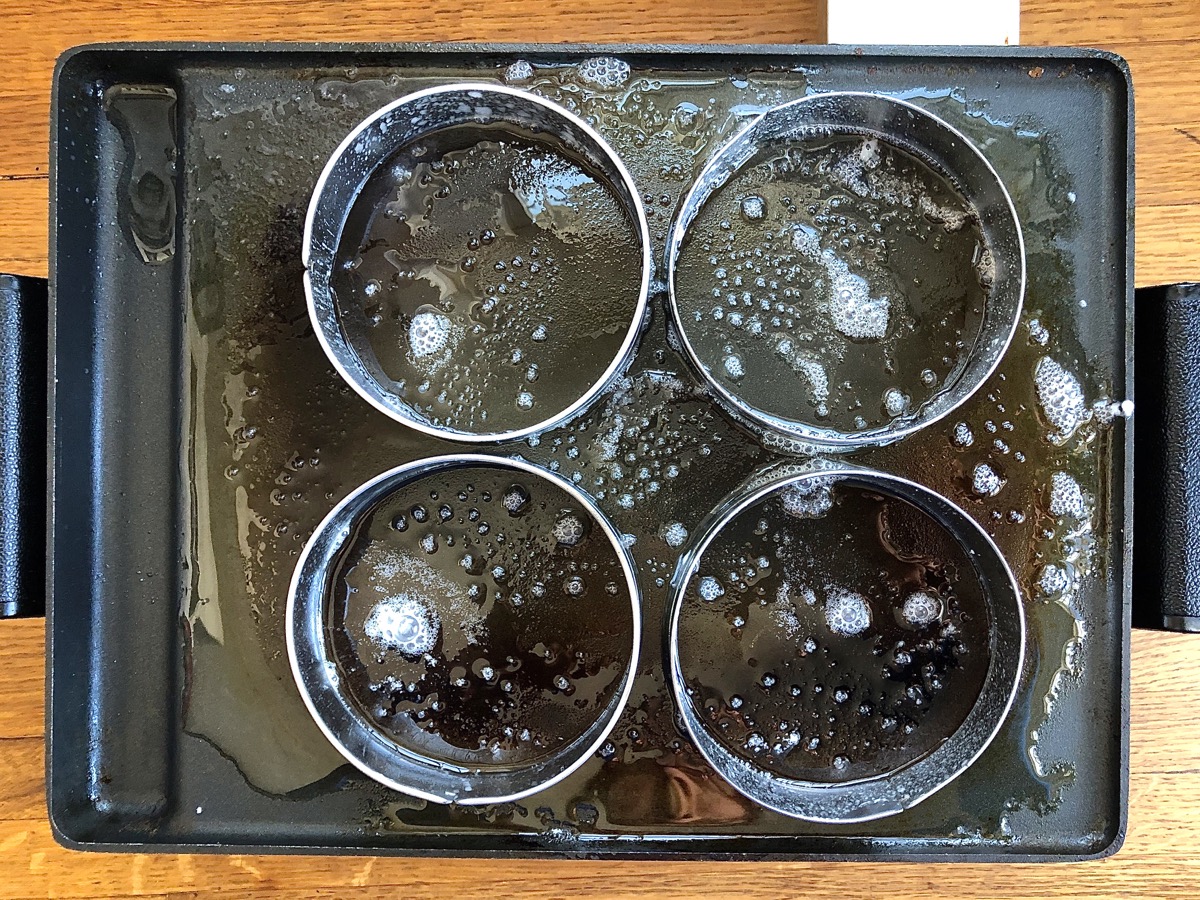 Hot griddle brushed with vegetable oil and butter, holding four English muffin rings.