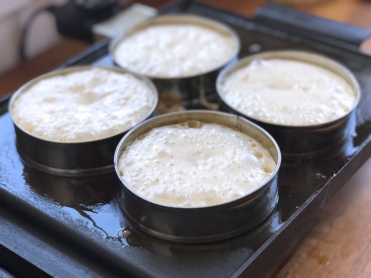 Four sourdough crumpets cooking on a griddle.