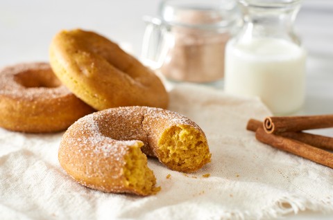 A few freshly baked cakey pumpkin donuts next to a glass of milk and a few cinnamon sticks. - select to zoom