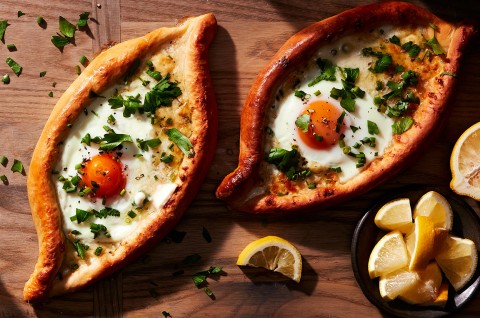 Two freshly baked Khachapuri (Georgian Cheese Breads) topped with soft-baked eggs and fresh herbs - select to zoom