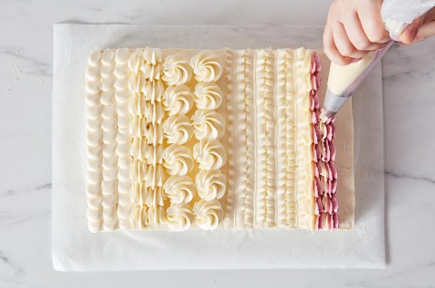 Hands piping designs on a sheet cake