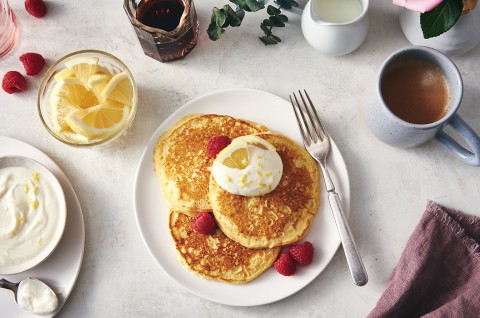 A stack of Lemon Ricotta Pancakes on a plate, topped with honey butter and garnished with slices of fresh lemon and berries.