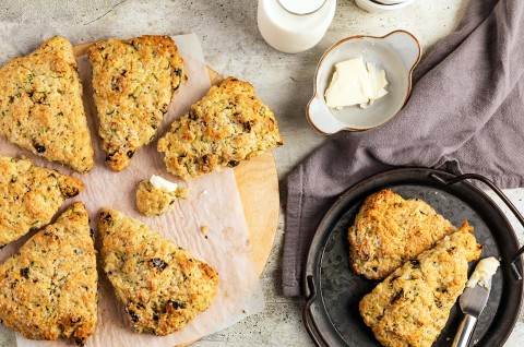 Zucchini scones on a piece of parchment paper with two on a small plate next to a bowl of butter - select to zoom