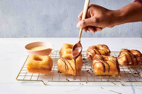 Hand adding chocolate glaze to doughnuts