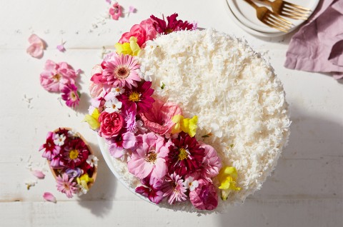 A whole Old-Fashioned Coconut Cake coated in shredded coconut and decorated with edible flowers - select to zoom