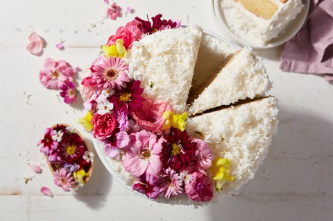 A Old-Fashioned Coconut Cake coated in shredded coconut and decorated with a spray of edible flowers - select to zoom