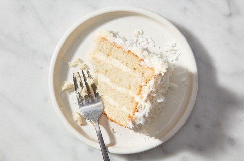 A single slice of Coconut Layer Cake on a plate with a fork - select to zoom