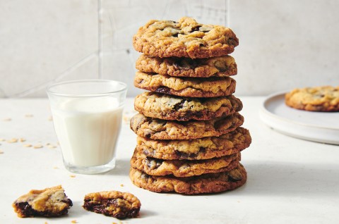 A stack of oatmeal chocolate chip cookies next to a glass of milk. The cookies have crisp golden brown edges and visible chocolate chips. - select to zoom