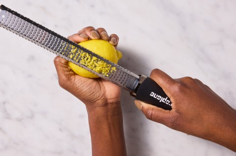 Hands zesting a lemon with a microplane zester