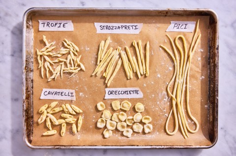 Different hand-shaped pasta types on a parchment-lined baking sheet