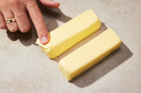 Baker placing their finger on two sticks of cold butter