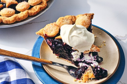 A slice of Fresh Blueberry Pie served on a plate with whipped cream - select to zoom