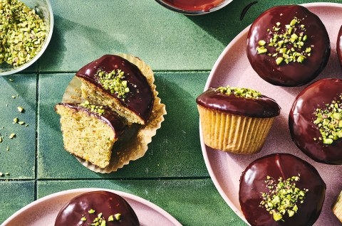 A Pistachio-Cardamom Cupcake with Dark Chocolate Ganache sliced in half and a bunch more on plates - select to zoom