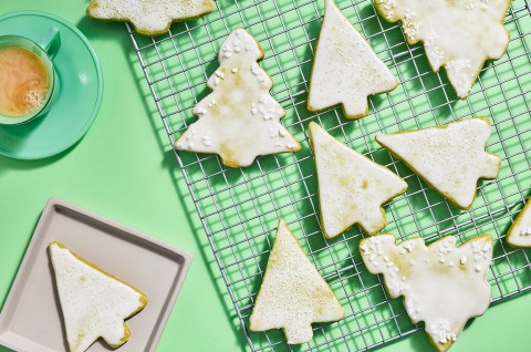 Christmas tree shaped cookies with a light white glaze spread out on a drying rack. - select to zoom