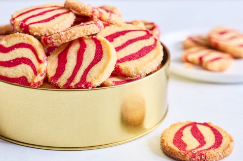 Striped peppermint shortbread cookies inside a gold cookie tin seen from the side. - select to zoom