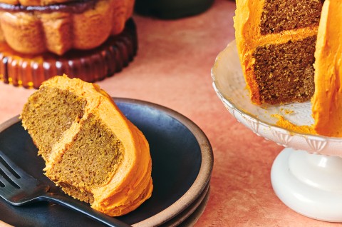 A slice of pumpkin bundt cake on a dark colored plate layered and covered with orange frosting. - select to zoom