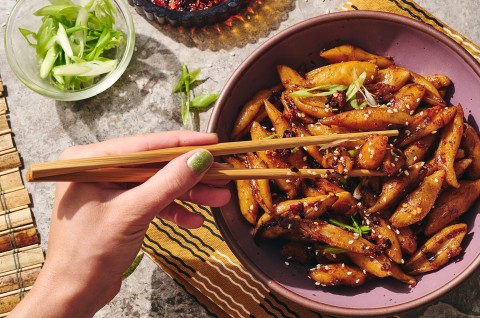 A person picking up hand cut noodles dressed with a dark umami sauce using chopsticks. - select to zoom