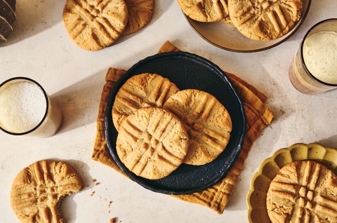 Classic Peanut Butter Cookies spread around a counter layout with some placed on a plate, others on decorative elements, and some on the counter itself. Glasses of milk are present too. - select to zoom