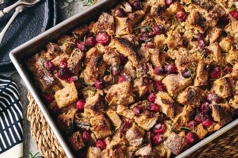 A photograph of the top of Cranberry-Rosemary Breakfast Pudding showing coarsely arranged and baked cranberries, bread, and roesmary. - select to zoom