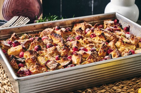 A photograph of the side of Cranberry-Rosemary Breakfast Pudding in a pan showing coarsely arranged and baked cranberries, bread, and roesmary. - select to zoom