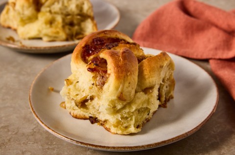 A French Onion Roll on a plate showing the golden brown exterior and lofty baked interior with caramelized onions. - select to zoom