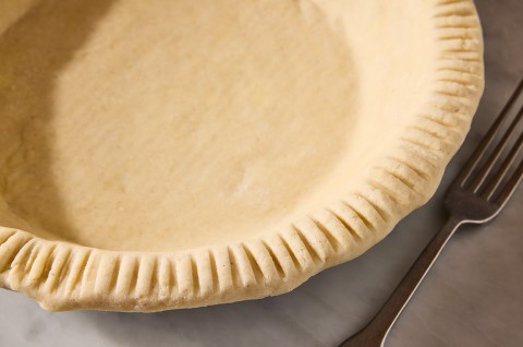 A gluten-free pie crust in a pie pan showing a smooth dough and a beautifully fork-crimped crust. - select to zoom