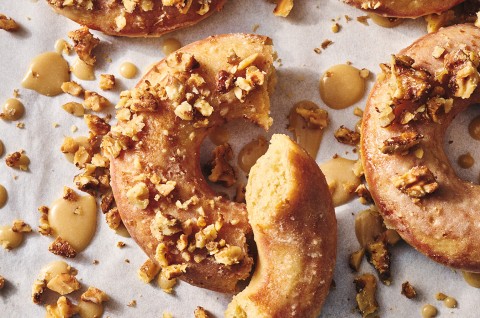 A broke maple donut with a moist and crumbly interior surrounded by dollops of glaze and broken nut meat. - select to zoom