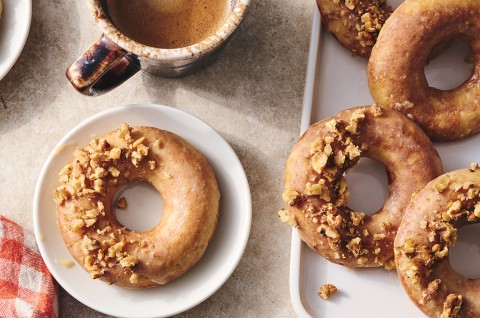 A Maple Donut on a plate with half coated in broke nut meat and the other half glazed. - select to zoom