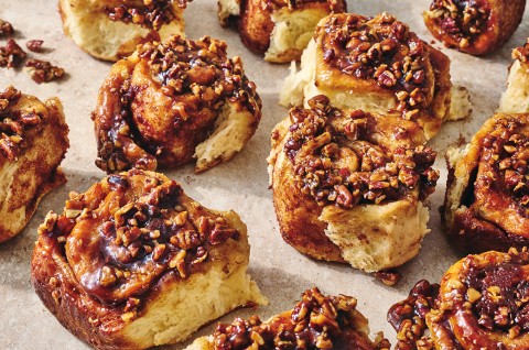 Multiple sticky buns separated on a counter top showing the golden interior and sticky glazed tops coated in nuts. - select to zoom