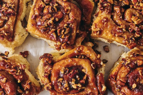 Overhead view of a tray of dark brown sticky buns fresh out of the oven and covered in nuts and glaze. - select to zoom