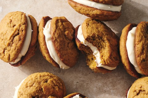 Pumpkin Whoopie Pies photographed together on a counter showing the layers of pumpkin cookie and creamy filling. - select to zoom