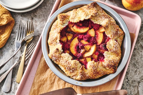 Photograph of Rustic Raspberry-Peach Pie from above with a perfectly browned folded crust around the edges of a vibrant raspberry and peach filling. - select to zoom