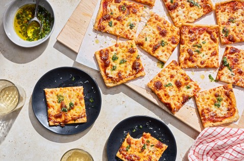 Slices of Gluten-Free Sheet Pan Pizza seen from above and randomly arranged on a cutting board with other slices on plates. - select to zoom