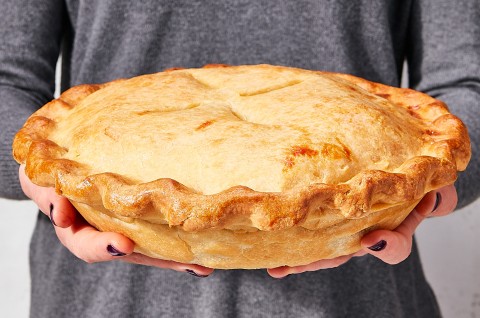 A person with a grey dress holding a large, perfectly golden, baked thanksgiving leftover pie. - select to zoom